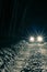 Sports car with high beam on in a winter pine forest at night, front and background blurred with bokeh effect