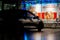 Sports car parked at night outside convenience shop reflecting vibrant coloured lights on windows