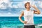 Sports drink fitness man drinking water botlle during outdoor exercise workout on beach. Dehydrated athlete runner after