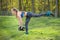 Sports girl in a blue tank top with black dumbbells in her hands performs an exercise against the backdrop of summer nature