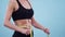 Sports woman measures waist in studio on blue background, a close-up. Concept of weight loss and diet.