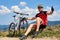 Sportsman bicyclist in sportswear and helmet sitting near his mountain bike on grassy roadside