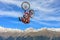 Sportsman biker flies in air with bicycle upside down from jump at bike competition on snowy Caucasus mountain peaks and blue sky