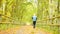 Sportsman in blue t-shirt and black trousers run on road. The man is slowly running on asphalt way covered by autumn leaves. Path