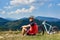 Sportsman cyclist in professional sportswear and helmet sitting near his bicycle on grassy roadside