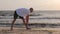 Sportsman stretching during morning exercises on seashore at sunrise