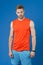 Sportsman on violet background. Muscular man in orange vest and blue shorts. Fit and confident. Sport fashion for