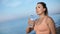 Sportswoman drinking water from bottle after outdoor training at beach. Medium shot on RED camera