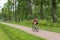 Sportswoman riding a bike on a path in the forest among the tall green trees in the summer, Cycling