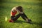 Sportswoman sit on green grass with gym equipment on summer
