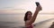 Sporty attractive woman standing with phone and shooting sunset or sunrise on the beach