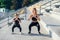 Sporty beautiful elder and younger sisters which squating together during fitness training outdoors.