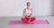 Sporty beautiful smiling woman sitting cross-legged on exercise mat in bright room or studio