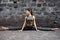 Sporty beautiful young woman practicing yoga hanumanasana working out, wearing sportswear, outdoor full length, brick wall backgro