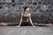 Sporty beautiful young woman practicing yoga hanumanasana working out, wearing sportswear, outdoor full length, brick wall backgro