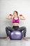 Sporty blond girl doing dumbbell exercise while sitting on fitball