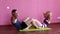 Sporty blonde girl and a bearded man pumping abdominal muscles in a fitness club on a pink background.