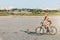 A sporty blonde woman in a colorful suit rides a bike at fast speed in a desert area on a sunny summer day. Fitness concept. Blur