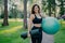 Sporty European woman in cropped top and leggings, carries rolled up karemat and fitness ball, going to have aerobics exercises,