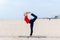 Sporty fit blond woman in red and dark blue sportswear working out outdoors on summer day, doing Natarajasana, Dancer