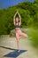 Sporty fit middle aged woman doing Hatha yoga, Vrikshasana asana, tree pose on tropical beach.