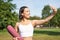 Sporty fitness girl takes selfie with rubber yoga mat in park, does workout and shares photos on social media