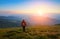 Sporty girl with back sack is standing at the lawn and watching on the endless cast of mountains landscape.