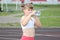 A sporty girl drinks water from a bottle and smiles sweetly at a running stadium