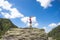 Sporty girl on a hiking trip is standing on a big rock and raises her hands in the air