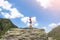 Sporty girl on a hiking trip is standing on a big rock and raises her hands in the air