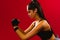 A sporty girl with long hair looks seriously to the side during physical exercises. Profile photo on a red background.