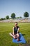 Sporty girl sitting on yoga mat getting ready for training on stadium green lawn. Sport, physical exercise