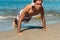 Sporty Latin man in headphones doing push-ups on seashore