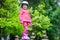 A sporty little girl in a helmet and protective gear stands on roller skates in a city park. Beautiful baby in a pink jacket and