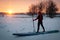 a sporty man in a red hat with a paddle stands on an inflatable board in the middle of the snow, winter sup board