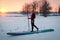 a sporty man in a red hat with a paddle stands on an inflatable board in the middle of the snow, winter sup board