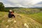 Sporty mature woman sits on top of a mountain and looks through binoculars at the Ural village, at the mountains, at the taiga, at