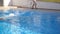 Sporty muscular man jumping in water of basin on sunny day. Young guy swimming in pool. Slow motion Close up