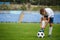 A sporty player with a football ball under his foot on a green grass on a stadium background. Hobby, activities concept.