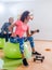 Sporty slim women taking part in gym fitness class exercising sitting on physioballs doing alternated biceps curl with