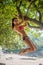 Sporty slim young woman wearing bikini climbing tree on a sandy beach at resort. Smiling caucasian brunette girl hangin