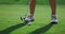 Sporty woman legs golfing at green course. Golfer train hitting ball on fairway.