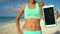 Sporty woman showing fitness training app running on phone screen on beach