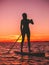 Sporty woman stand up paddle boarding at dusk on a flat warm quiet sea with beautiful sunset