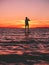 Sporty woman stand up paddle boarding on a flat warm quiet sea with bright sunset