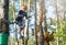 Sporty, young, cute boy in white t shirt spends his time in adventure rope park in helmet and safe equipment in the park