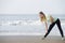 Sporty young woman bend down stretching at the beach