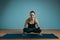 Sporty young woman doing stretching. Slim girl practicing yoga indoors on blue background. Calm, relax, healthy