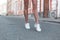 Sporty young woman with slender tanned legs in stylish white sneakers walks down the street. Fashionable women`s shoes. Summer