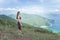 Sporty young woman standing on hill admiring the view of sea and green mountains in sunlight